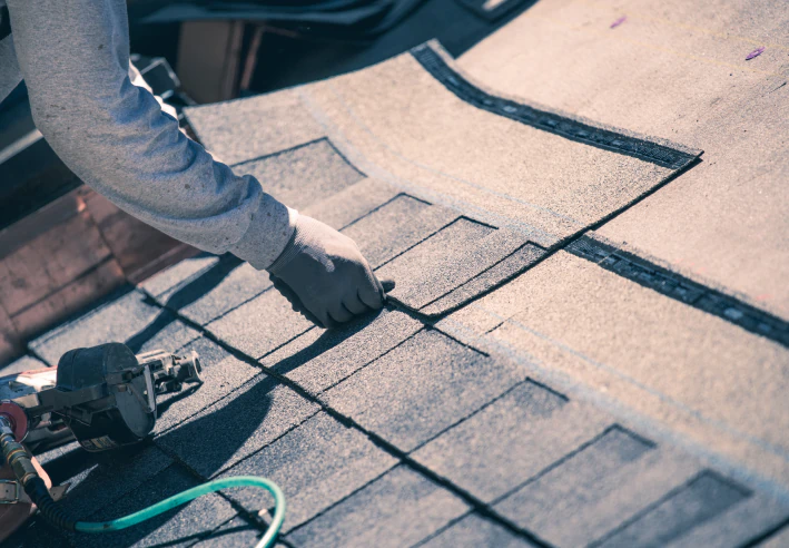 close up shot of worker installing new asphalt roof shingles
