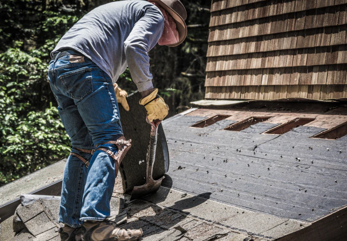 worker removing the old asphalt roof shingles